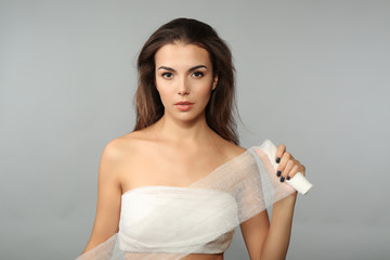 Young beautiful woman with a bandage on her chest, holding gauze, on grey background