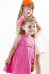  The older sister on the white dress takes care of the younger on the pink dress combing her hair and gets lipstick on her lips isolated on the white background