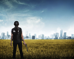 Police woman looking the city in the middle of field