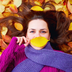 young girl lying among autumn leaves, hiding lips behind a leaf