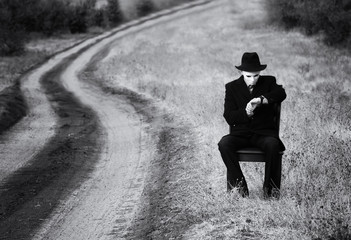 Man in the mask sitting on a chair by the side of the country road, black and white shot