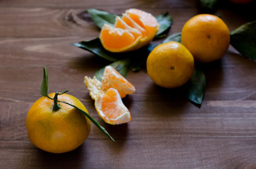 Мандарины с листьями и дольки мандарина на деревянном фоне