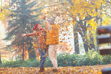 Smiling couple throwing leaves and having fun in autumn park