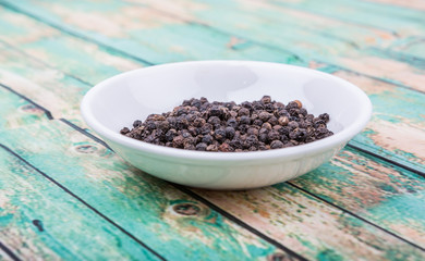 Black peppercorn in white bowl over wooden background