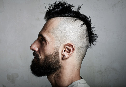Portrait of a bearded man with mohawk. Concrete background