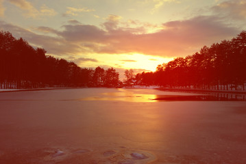 Beautiful colorful winter sunset above frozen mountain lake, with dramatic red sky. Image filtered in faded, washed out, retro style with soft focus.