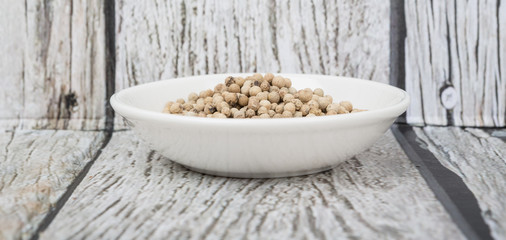 White peppercorn in white bowl over wooden background