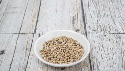 White peppercorn in white bowl over wooden background