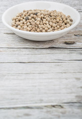White peppercorn in white bowl over wooden background