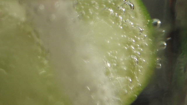 Macro ECU CU lime slice in a glass of tonic being poked and moved by a straw
