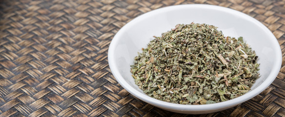 Dried lemon balm leaves in white bowl over wicker background