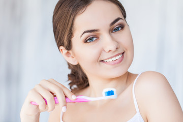 Beautiful smiling woman holding a toothbrush and toothpaste, fresh studio portrait