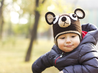 Joyful child in a cap in the form of teddy bear. Happy Child on a walk. The child is in the air in the fall
