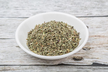 Dried lemon balm leaves in white bowl over wooden background