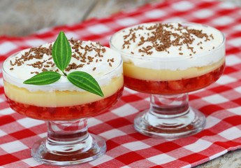 Trifle in dessert glasses on red and white checkered cloth on rustic wooden surface
