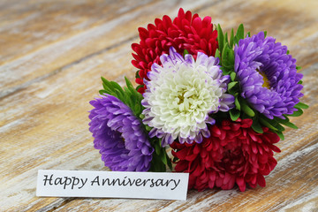 Happy Anniversary card with colorful bouquet of aster flowers on rustic wooden surface
