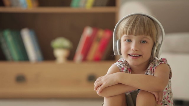 Cute little girl in headset listening to music singing and smiling at camera