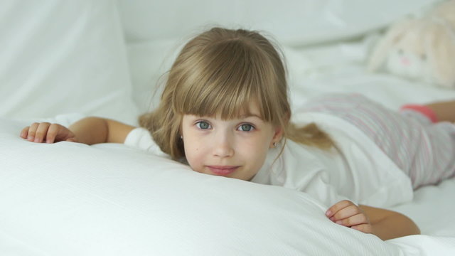 Cute little girl lying in bed and smiling at camera