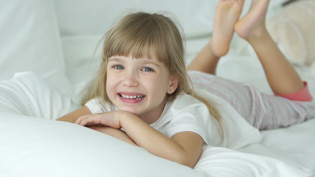 Funny little girl lying in bed smiling and laughing