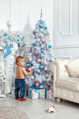 Obraz na płótnie Canvas Baby girl standing near the Christmas tree and holding decorations