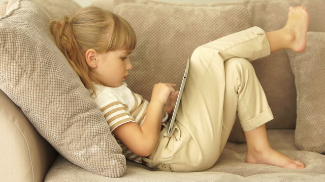 Little girl lying on sofa with tablet and smiling