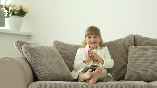 Little girl sitting on sofa with tablet and laughing