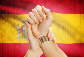 Barcode ID number on wrist and national flag on background - Spain