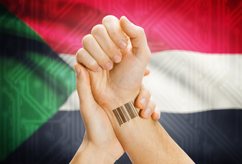 Barcode ID number on wrist and national flag on background - Sudan