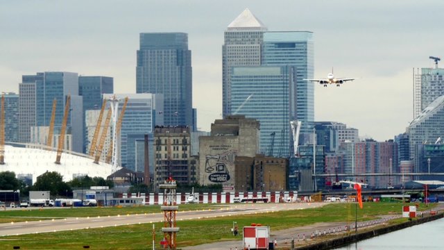 Airplane landing at City airport in London with skyscrapers in the background