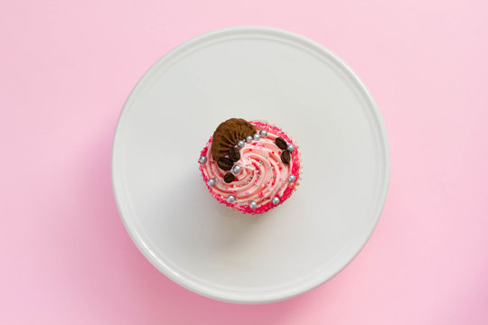 Pink decorated cupcake on white cake stand and pink background, top view, minimal style.