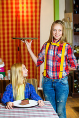 Happy cute smiling girl waiter holding a tray and standing near visitor