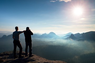 Two friends. Hiker thinking and photo enthusiast takes photos  stay on cliff. Dreamy fogy...