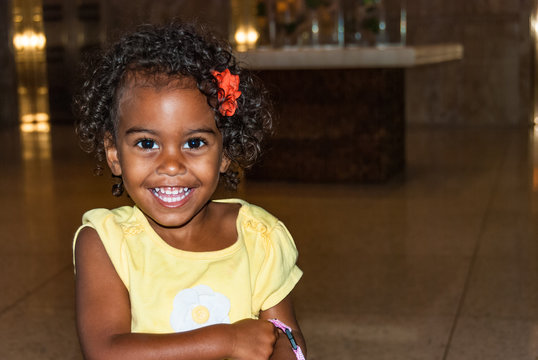 Beautiful young female girl with curly hair wearing a yellow t-shirt. Portrait of happy little child in front of brown background, pefect for family blogs and magazines