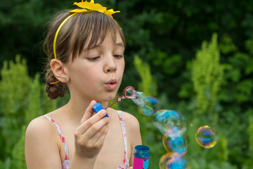 Little girl inflates soap bubbles in the garden