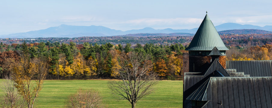 looking out at landscape of autumn woods with the Green Mountains of Vermont in the distance and the corner of the historic Farm Barn at Shelburne Farms a National Historic Site 
