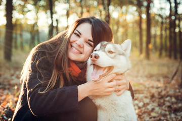 young happy female having fun with siberian husky dog in autumn park during sunset