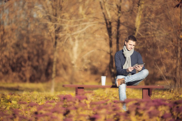 Young man drinking coffee with phone in autumn park  outdoors