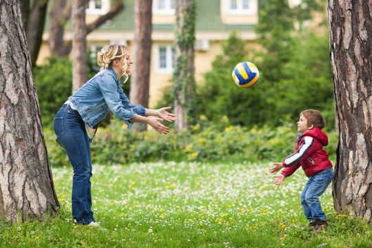 Young mother throwing a ball to her cute little son while playing in a park