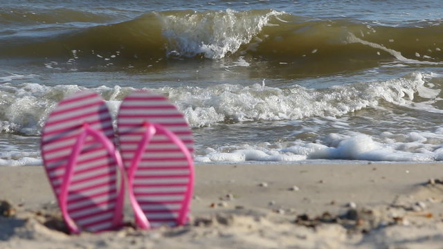 Pink flip flops blurred, against the backdrop of the waves