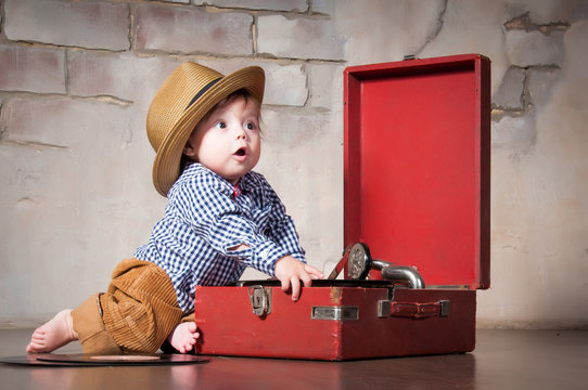 Funny baby boy in retro hat with vinyl record and gramophone