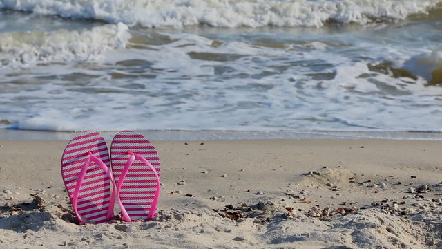 Pink flip flops on yellow sandy beach near sea waves, nobody.