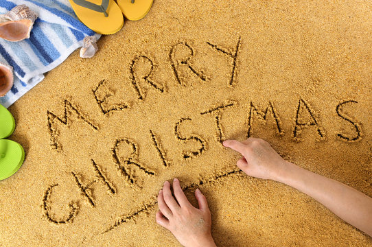 Child hand writing Merry Christmas message word written in sand on a sunny tropical beach winter holiday vacation photo