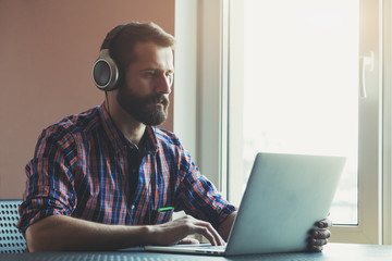 bearded man  in headphones listening to music with laptop
