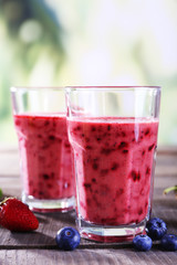 Glasses of berry smoothie on wooden table on blurred background