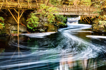 Little Bushkill creek meanders through the forest and leaves long exposure foam trails under wooden...