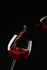 Poster Vin Red wine pouring into wine glass on black background