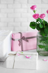 Composition of colourful gift boxes and flowers in glass on white table in front of brick wall background