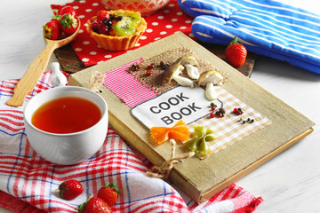 Obraz na płótnie Canvas Decorated cookbook with cup of tea and tasty cake on the table