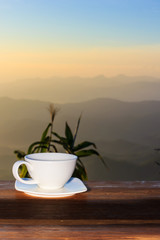 Cup of coffee on a wooden table in morning over mountain.