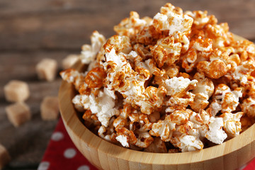 Sweet caramel popcorn in a bowl on red cotton napkin against wooden background